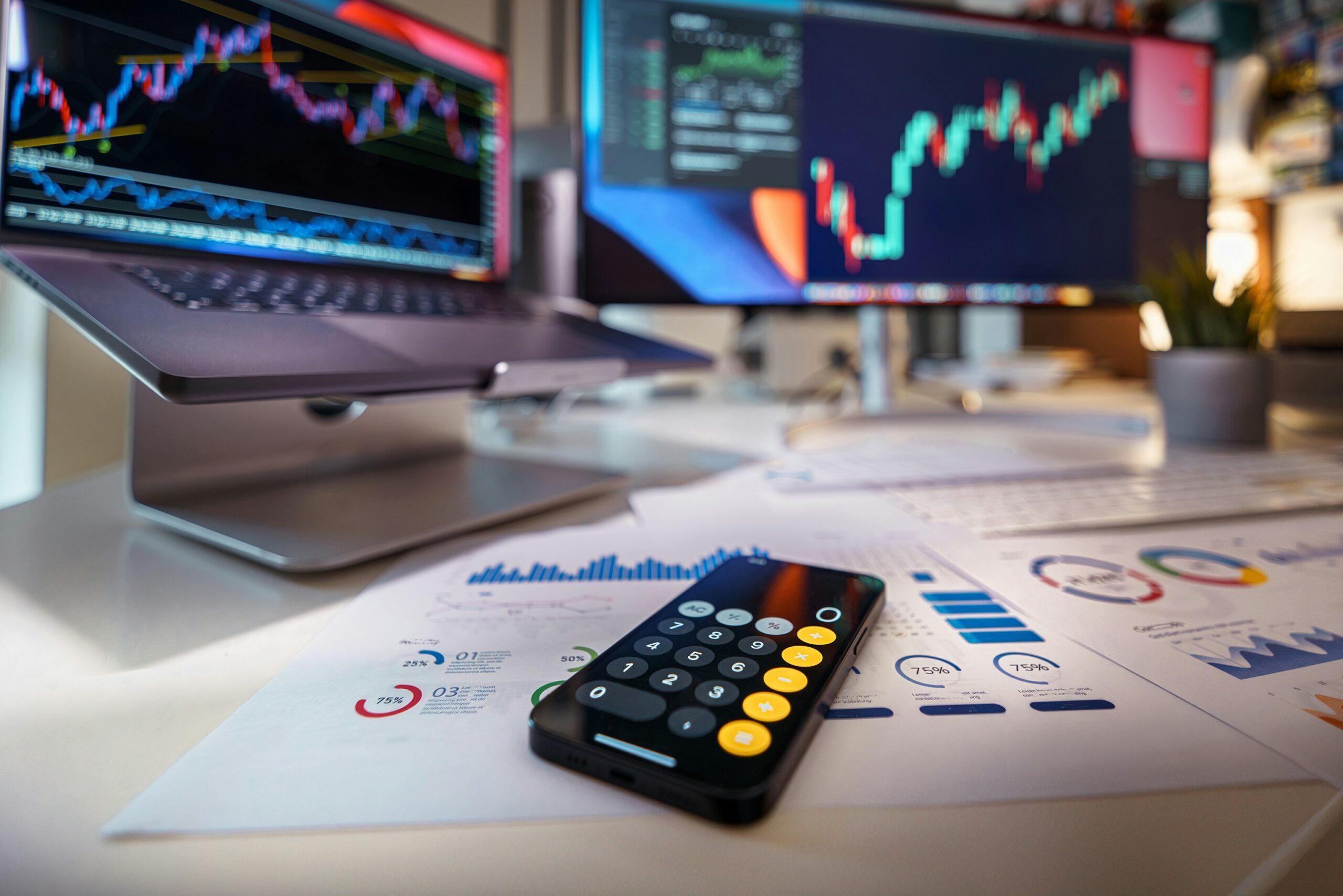 Calculator resting on paperwork with laptops displaying graphs in the background, symbolizing analysis and decision-making in real estate investing.