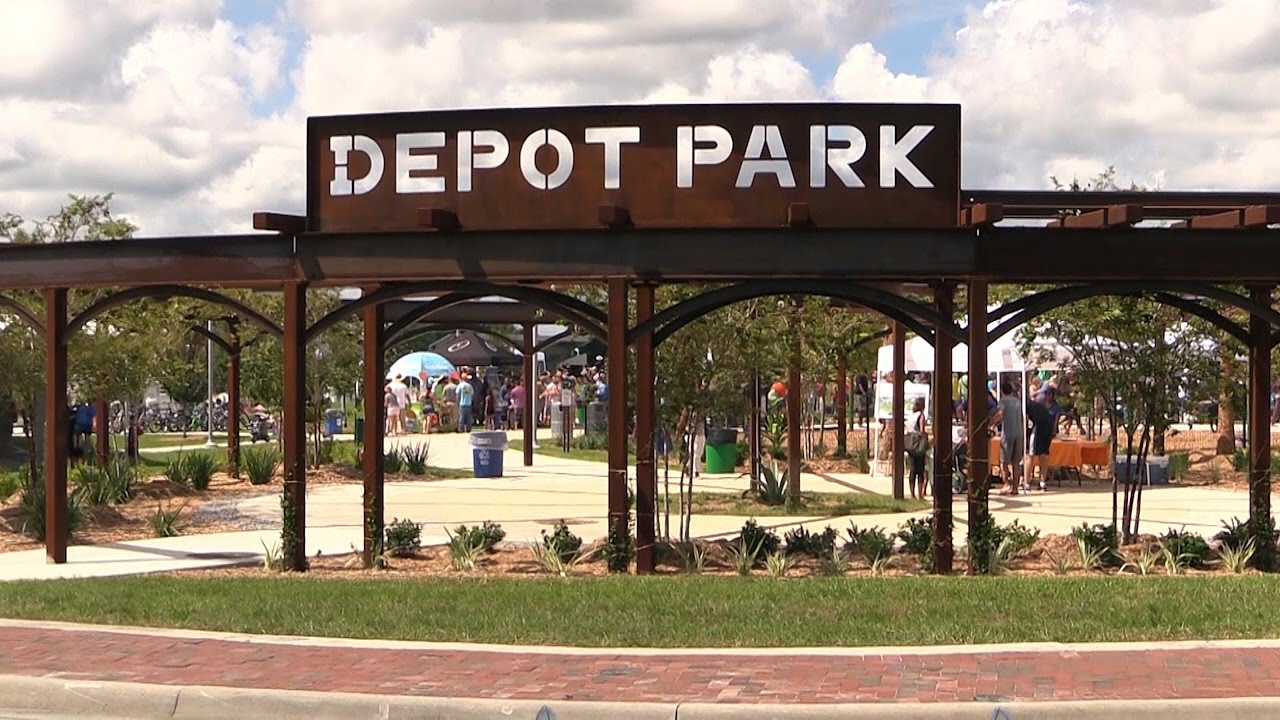 Entrance sign to Depot Park in Gainesville, FL with minimal landscaping, showing the park, people, and trees in the background