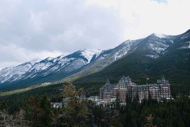 The Fairmont Banff Springs Hotel, a majestic castle-like structure, surrounded by tall trees and nestled against a backdrop of rugged mountain ranges.