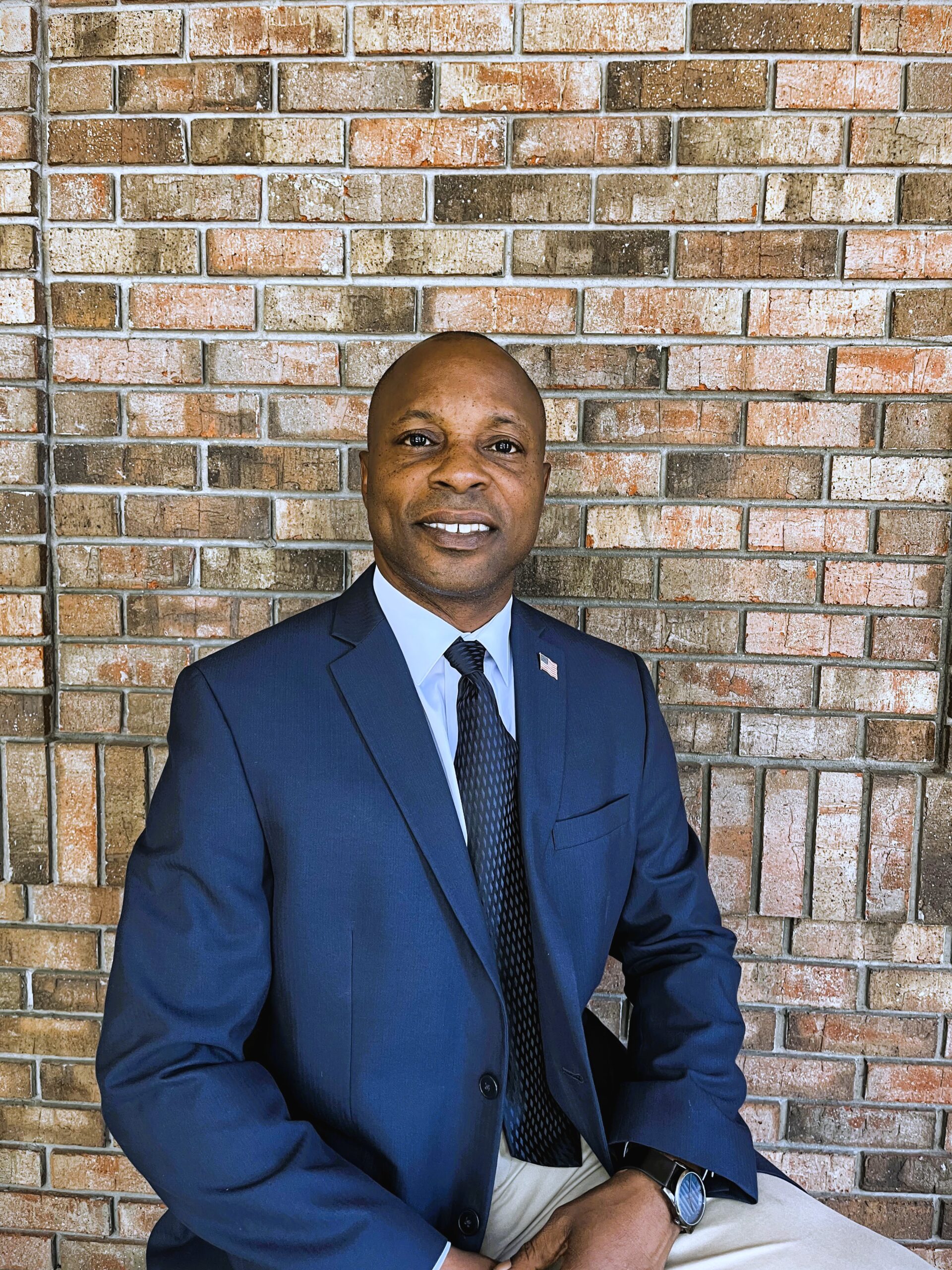 Realtor Jonathan Sherrod of Gainesville Realty seated in a blue suit jacket against a brick wall, presenting a confident and welcoming demeanor.