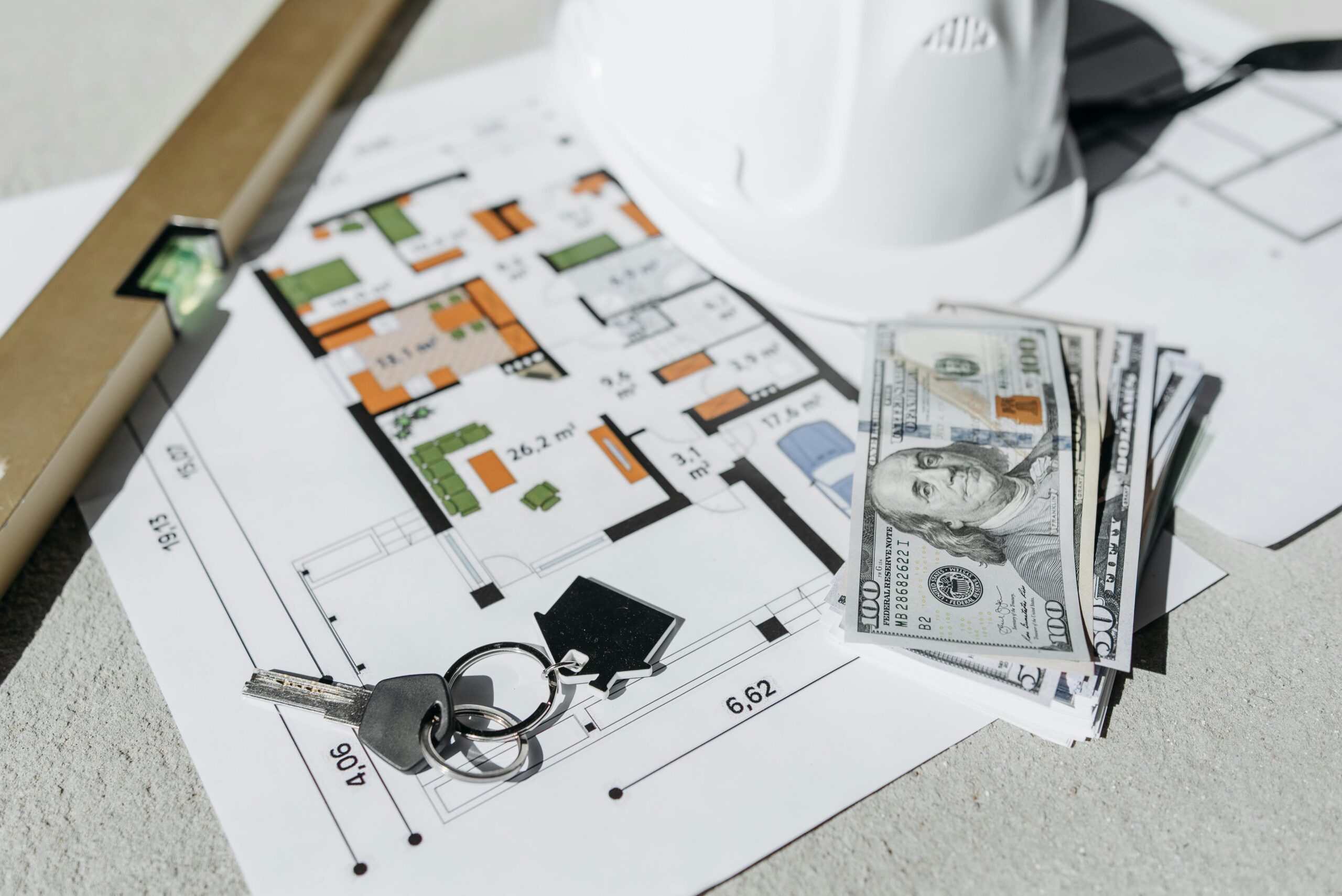 Construction plans laid out with a level, hardhat, house keys, and money, symbolizing real estate development and property investment.