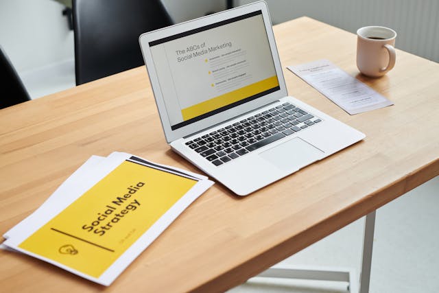 Table with a cup of coffee, laptop displaying marketing content, and a paper titled 'Social Media Strategy,' representing digital marketing strategies for real estate businesses.