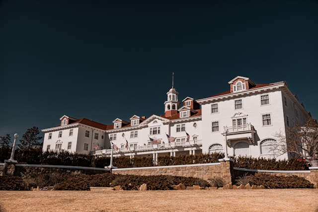 The Stanley Hotel stands tall surrounded by bare trees and other greenery, reflecting a serene fall/winter atmosphere under a clear sky.