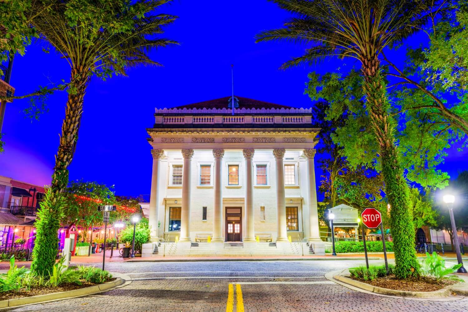 Hippodrome Theater in Gainesville, FL illuminated at night, framed by two large palm trees, showcasing the vibrant cultural hub in the community and its architectural charm.